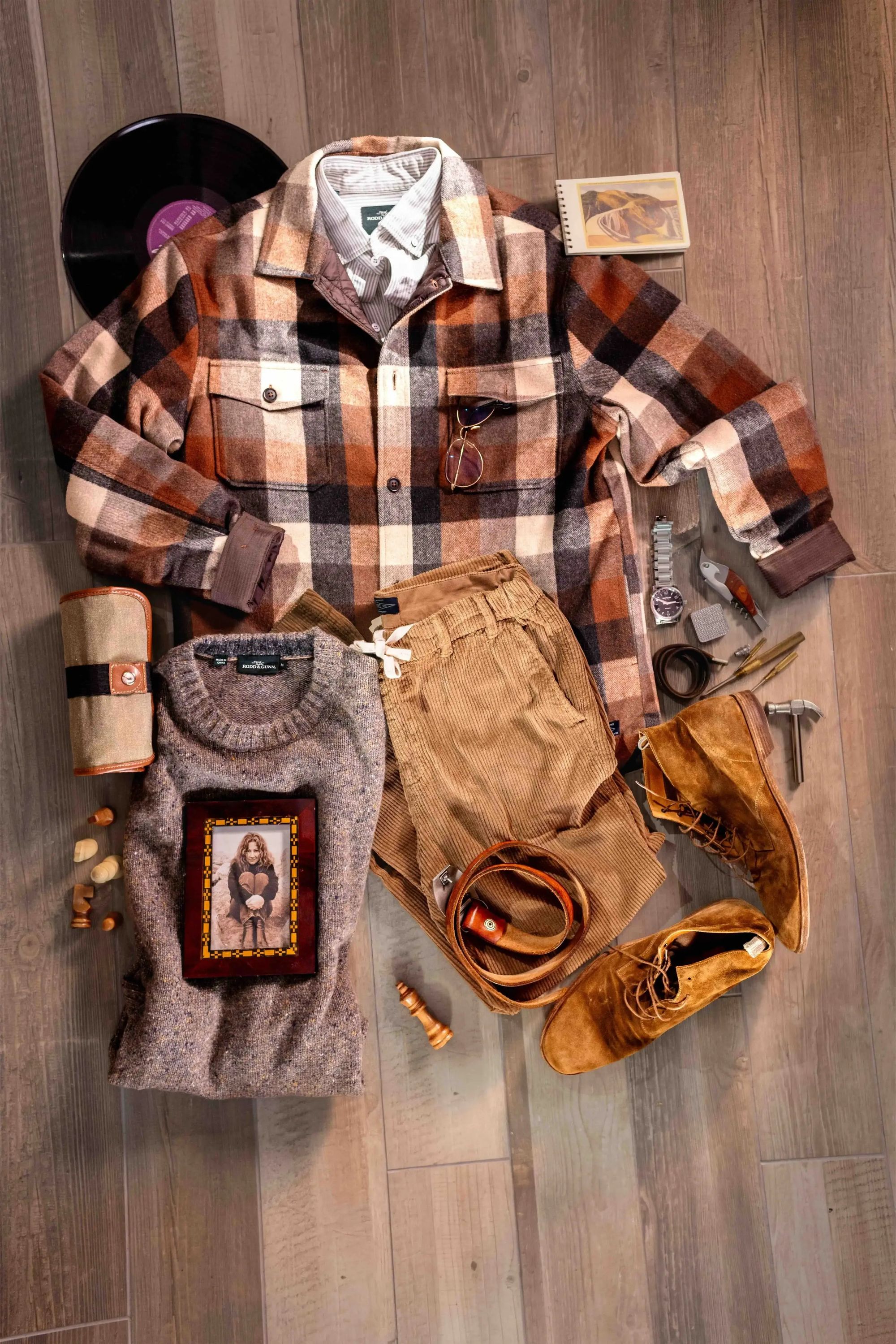 HANK plaid overshirt, knitwear and leather boots arranged on a table